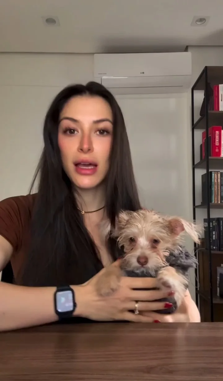 Deborah Moss falando para a câmera com sua cachorrinha no colo, à mesa de trabalho